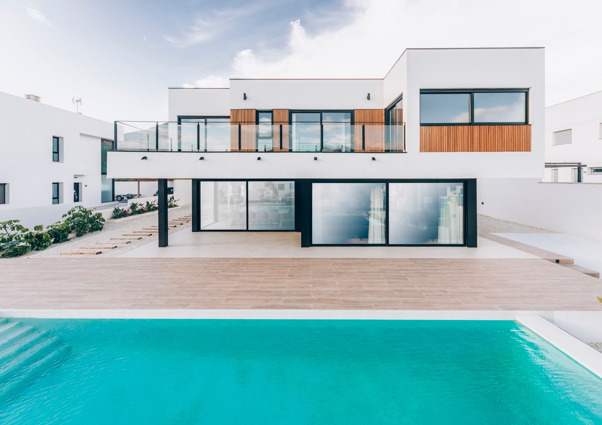Casa contemporánea de dos plantas con fachada blanca, detalles de madera y piscina; referencia de Modular Projects